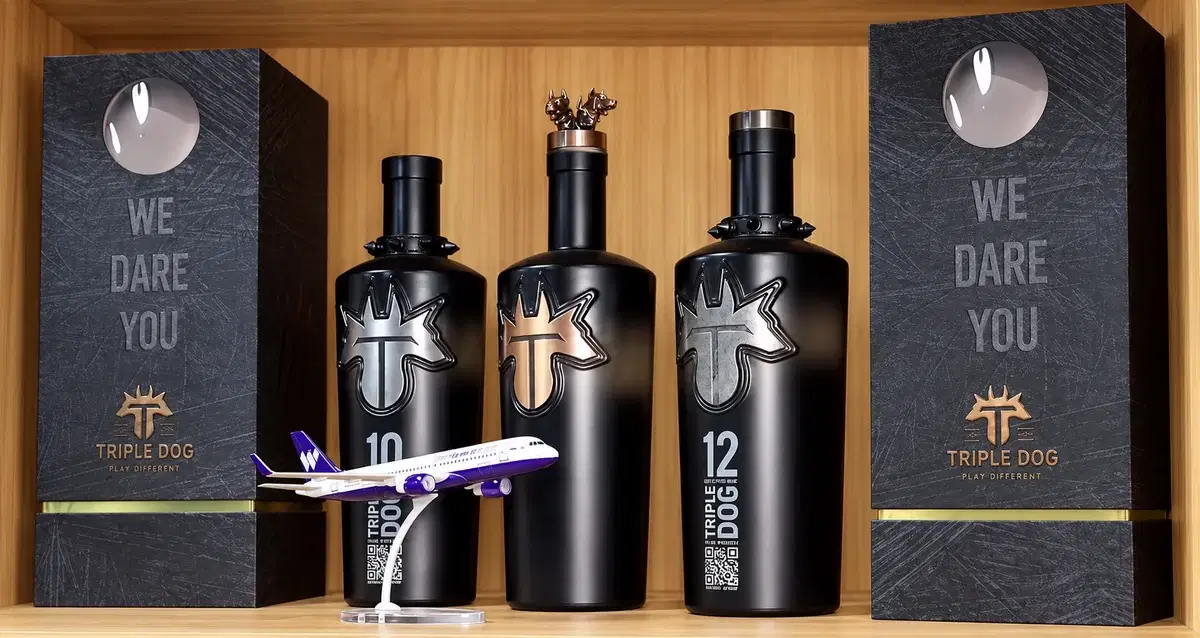 Triple Dog 10 and 12 whiskey bottles in matte black with metal dog-head emblems, between two "We Dare You" presentation boxes
