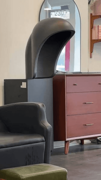 Matte black hooded salon dryer on a stand next to a wooden dresser